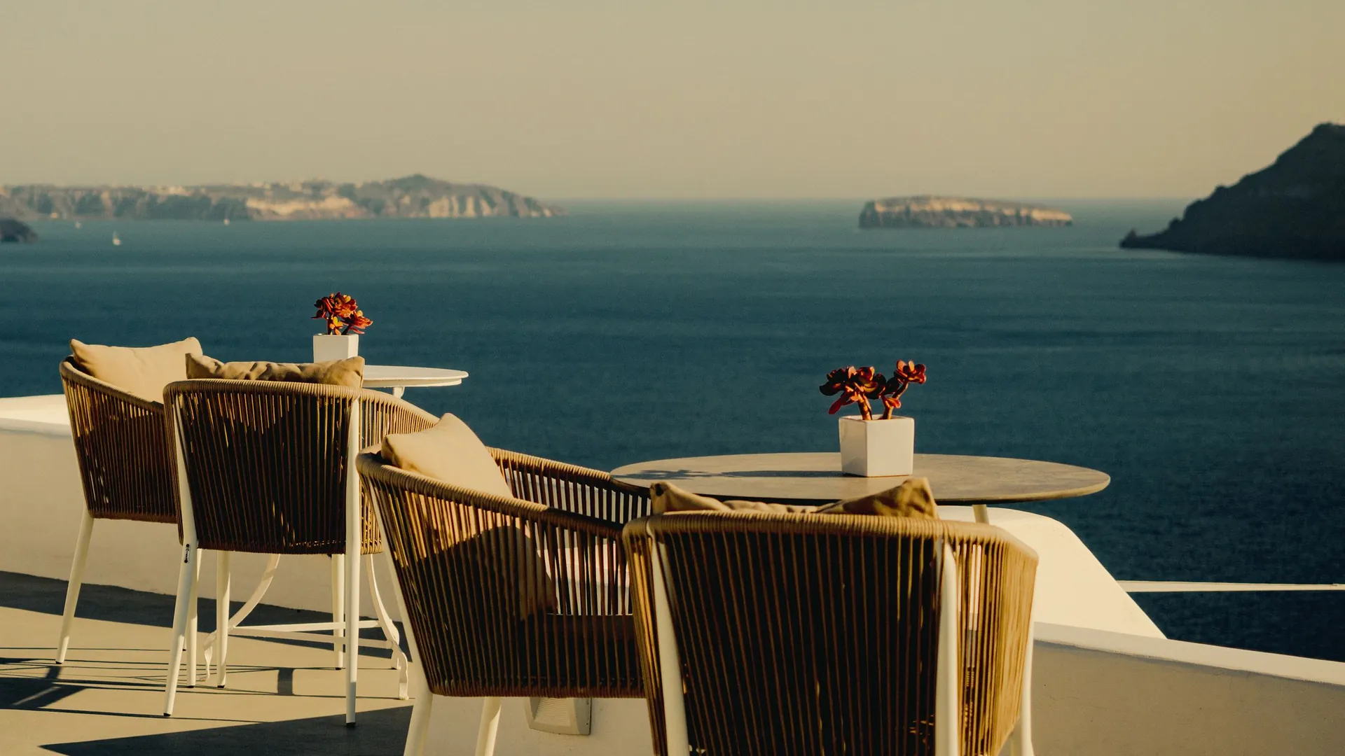 A quiet sea-view terrace at golden hour, tables set above deep blue water